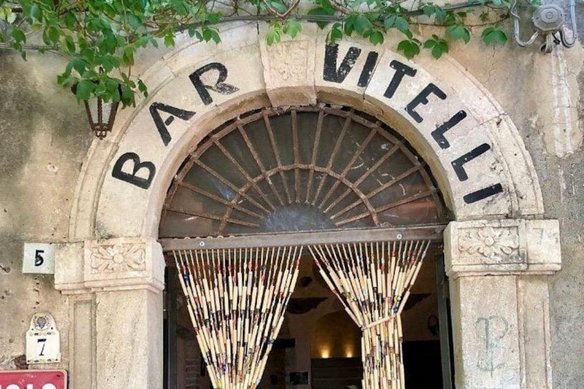 An entrance with a sign that reads 'BAR VITELLI' above a large arched doorway. 1