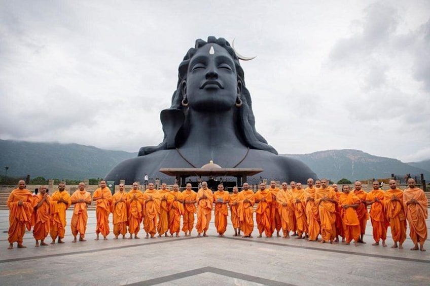 En gruppe mönke i orange klæder står foran en stor statue. 3