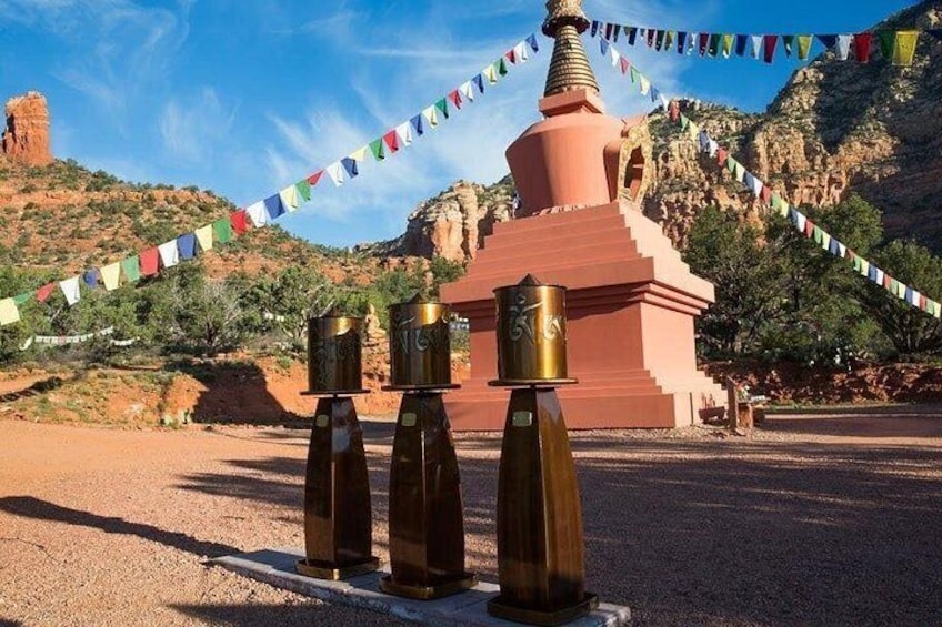 A pink stupa with prayer flags, surrounded by rocky terrain and a clear sky. 5