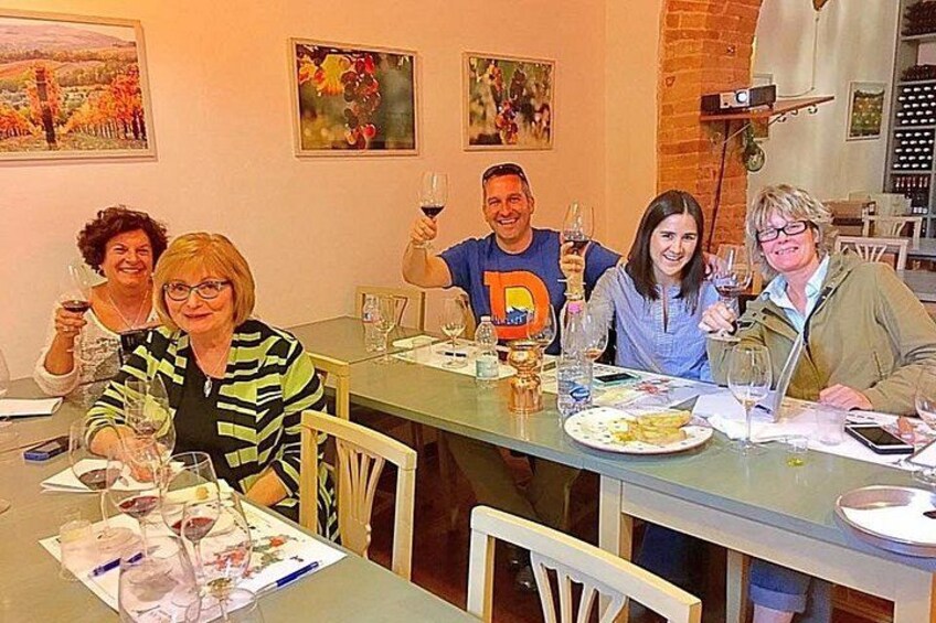 Un groupe de personnes est assis autour d’une table, devant des verres à vin, des assiettes remplies de nourriture et une bouteille de vin. 2
