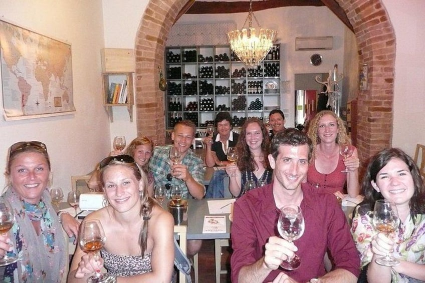 A group of people at a wine tasting event in a brick-walled room with wine bottles on shelves. 1