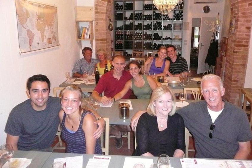 Un grupo de personas sentadas en una mesa en un restaurante, con una cava de vinos al fondo. 4