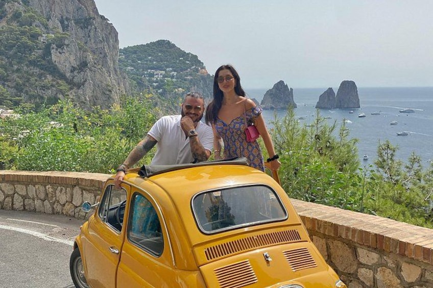 A yellow vintage car parked on a coastal road with a scenic view of cliffs and the sea. 3
