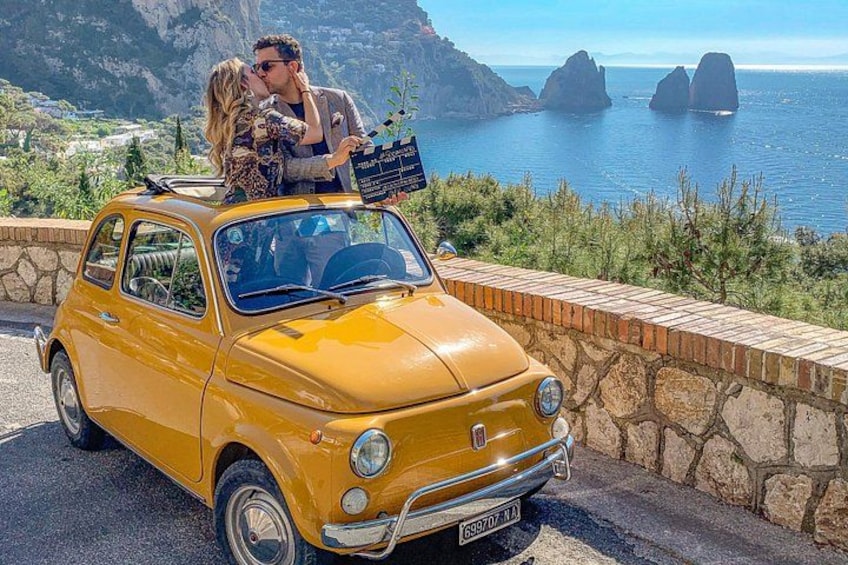 A yellow vintage car parked on a road with a scenic coastal backdrop. 1