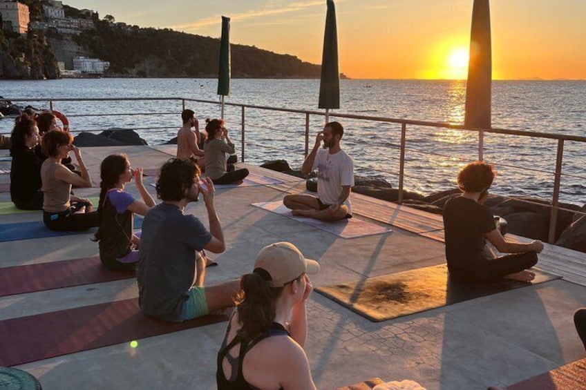 People sitting on mats outdoors during sunset by the water. 2