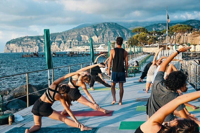 People performing yoga on a dock with a coastal landscape in the background. 1