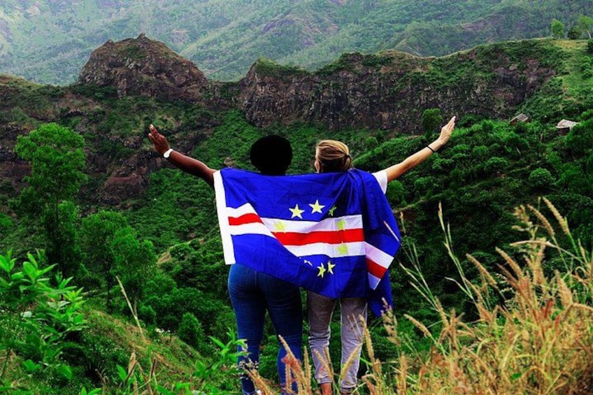 Two people standing on a hill with arms raised, holding a flag. 1