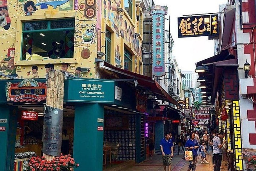 Une rue animée, bordée d’immeubles aux couleurs vives, avec une enseigne indiquant « CHY CREATIONS » et des passants. 5