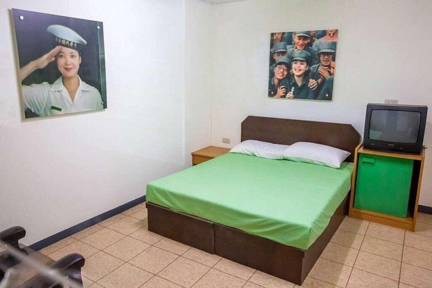 A bedroom with a bed, a television on a wooden stand, and two posters on the wall. 3
