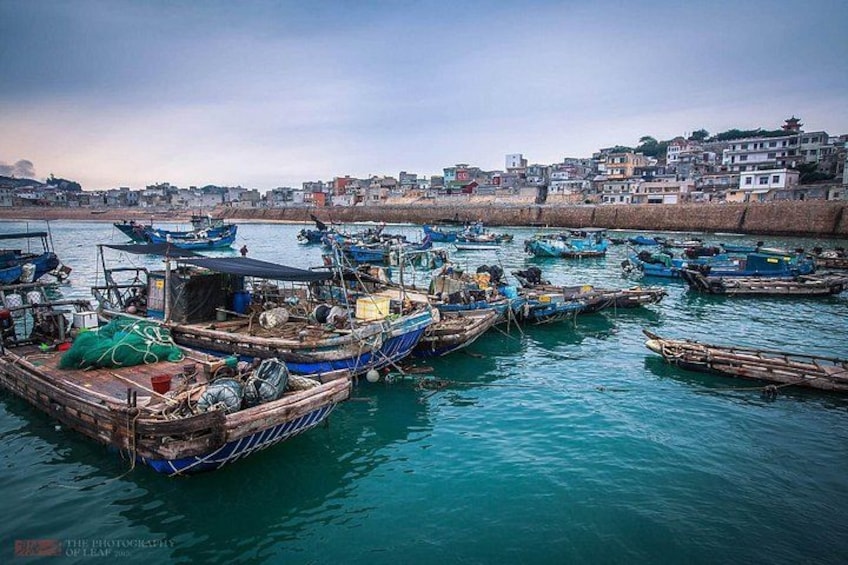 A harbor with numerous boats docked, a calm sea, and a cityscape in the background. 3