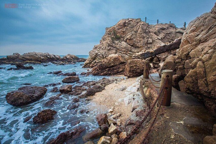 A rocky coastline with waves crashing against the shore, a metal railing, and a clear sky. 2