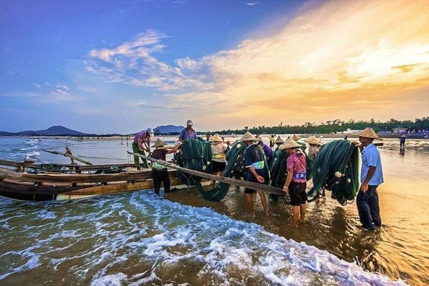 People in traditional attire near a boat on a calm body of water with a sunset in the background. 4