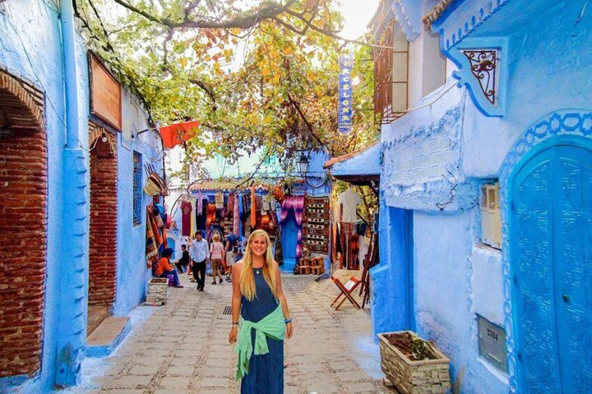 A narrow street with blue-painted buildings, a person standing in the foreground, and a shop in the background. 3