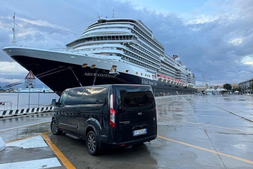 A cruise ship docked at a port with a black van parked in front. 1