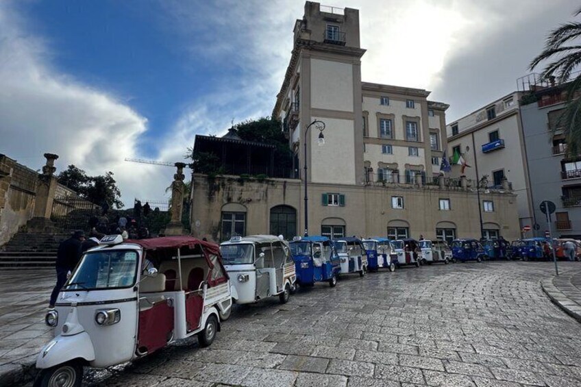 A cobblestone street with vintage vehicles parked in front of a historic building. 4