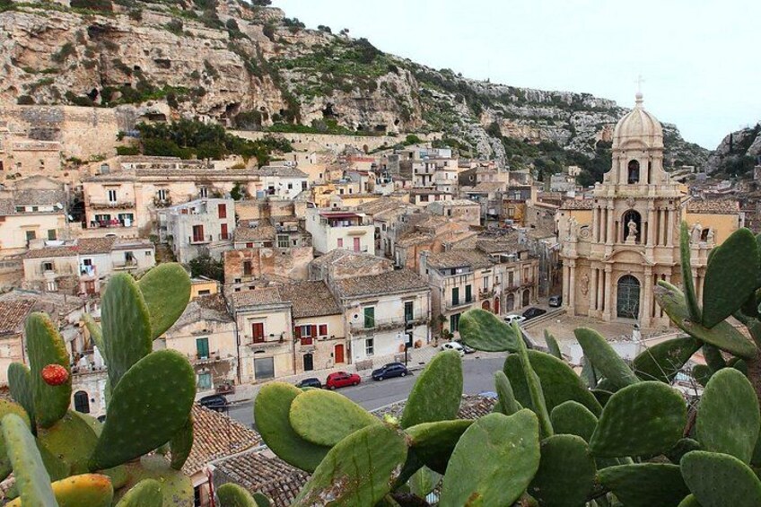 A coastal town with a prominent church, cacti in the foreground, and rocky cliffs in the background. 3