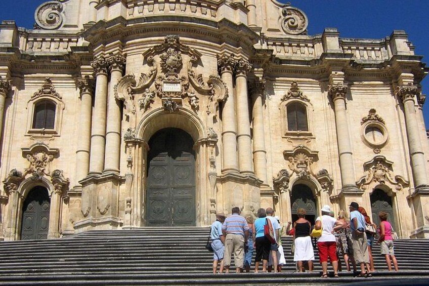 A historic building with ornate architecture, a large central door, and steps leading up to it. 2
