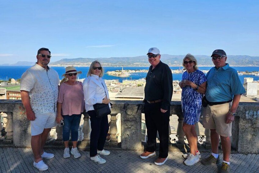 A group of people standing on a terrace overlooking a coastal cityscape. 5