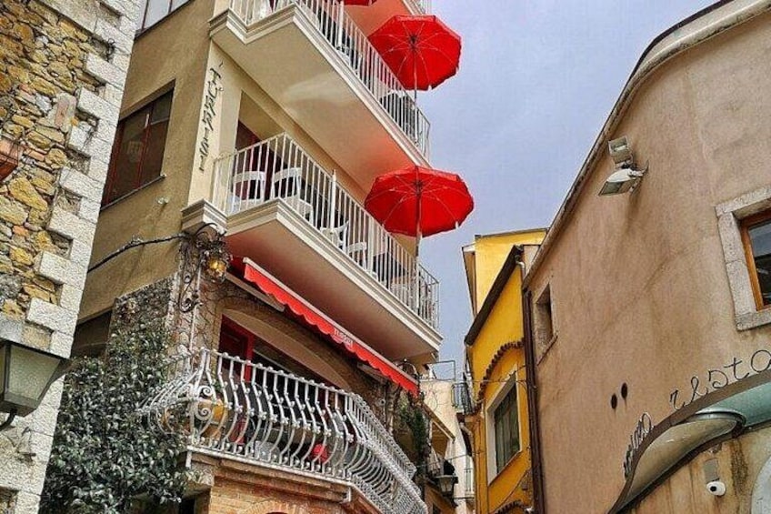 A narrow street with buildings, balconies, and red umbrellas. 3