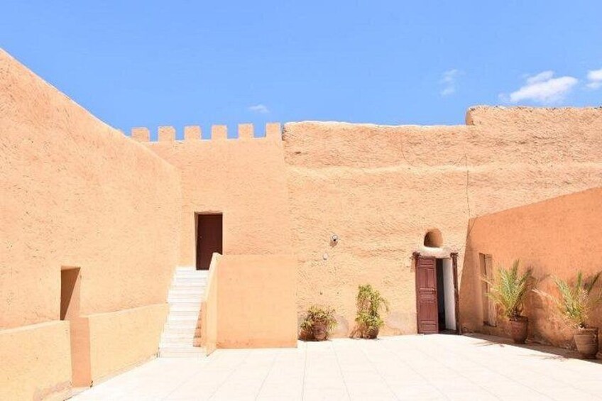 A desert courtyard with a staircase leading to a door, surrounded by walls and potted plants. 3
