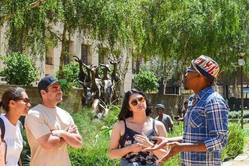 A group of people standing outdoors, a statue of deer in the background, and a person gesturing. 2