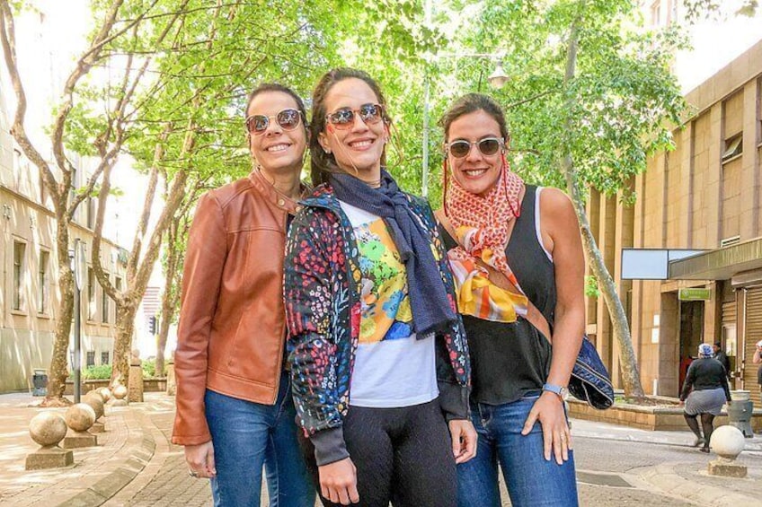 Three people standing on a sidewalk with trees and buildings in the background. 3