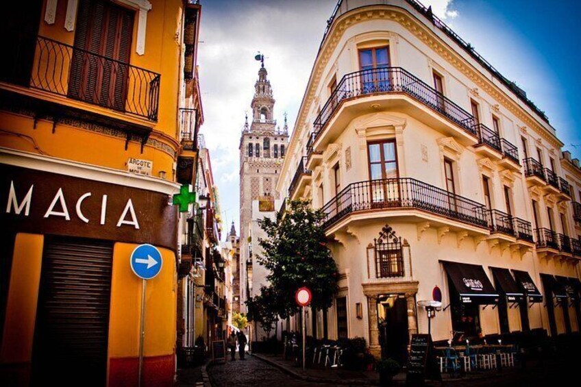 A street with buildings, a sign for 'MACIA', and a church spire in the background. 5