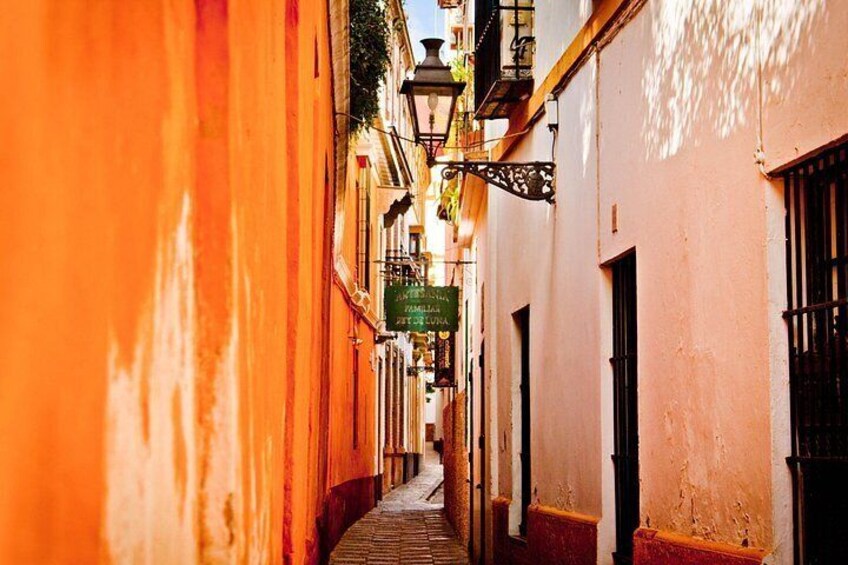 A narrow street with buildings painted in warm tones, a hanging sign, and a street lamp. 2