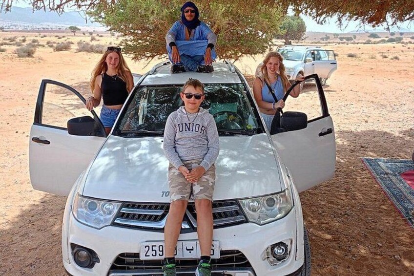 A white SUV parked in a desert with three people standing on it. 2