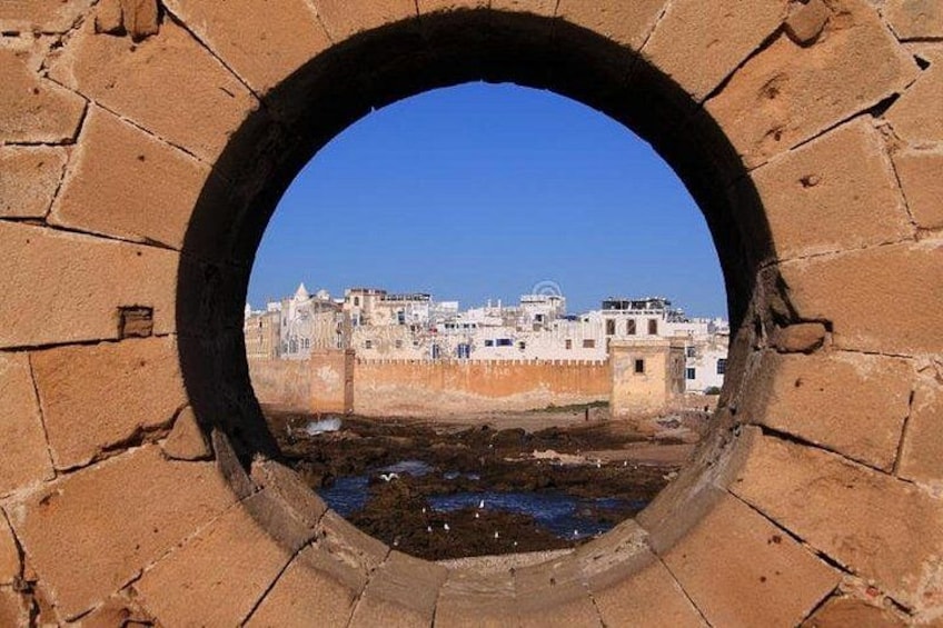 Une fenêtre circulaire en pierre offrant une vue sur un paysage urbain et une étendue d’eau. 2