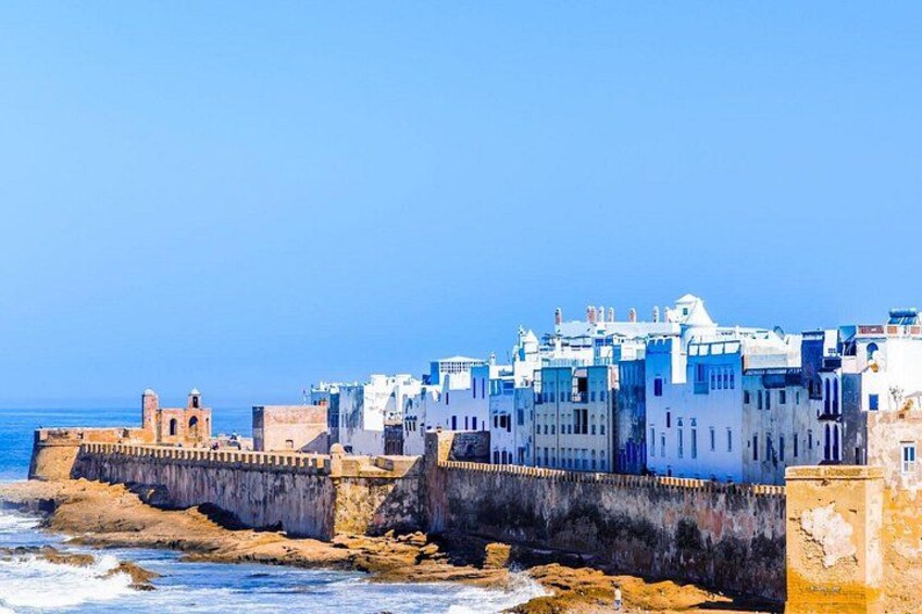 Une ville côtière aux bâtiments blancs, dotée d’une digue et surplombée d’un ciel bleu azur. 3
