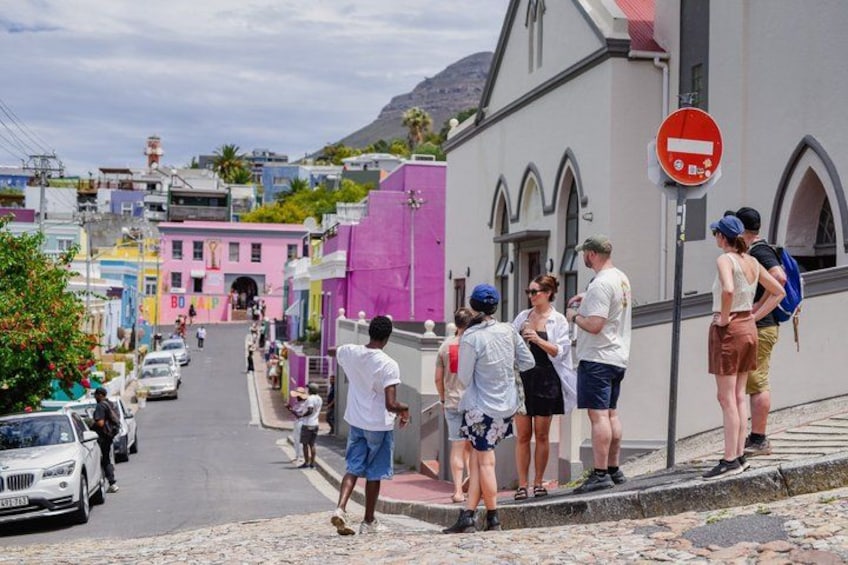 Une rue bordée d’immeubles aux couleurs vives, un panneau indiquant l’interdiction de circuler, et des personnes debout sur le trottoir. 1