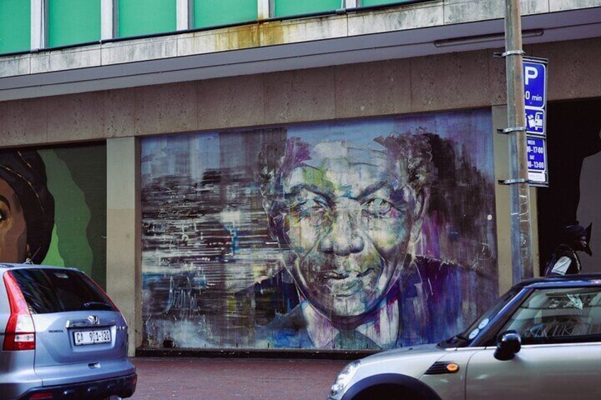 Une fresque sur un bâtiment, un panneau de signalisation pour un parking et une voiture. 2