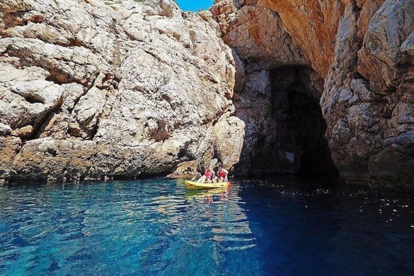 A rocky coastline with a cave entrance and a small yellow boat with people. 1