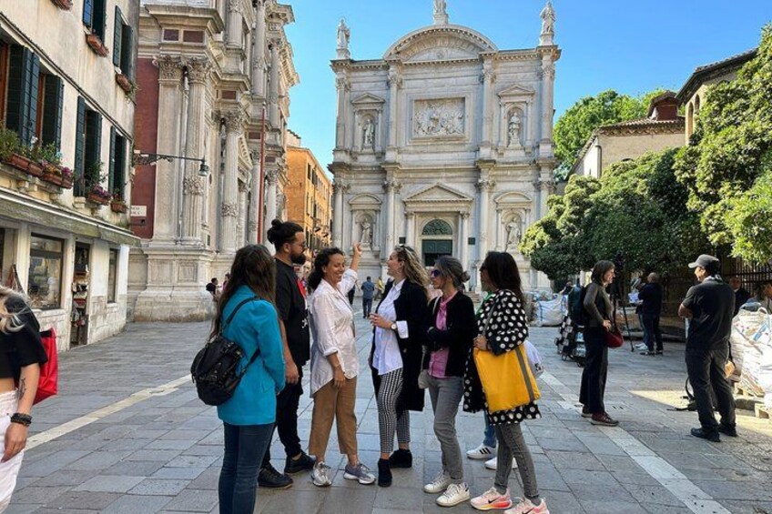 Eine Gruppe von Touristen steht auf einem Platz, im Hintergrund ein historisches Gebäude. 3