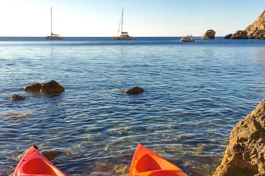 A calm sea with rocks and kayaks, sailboats in the distance. 2
