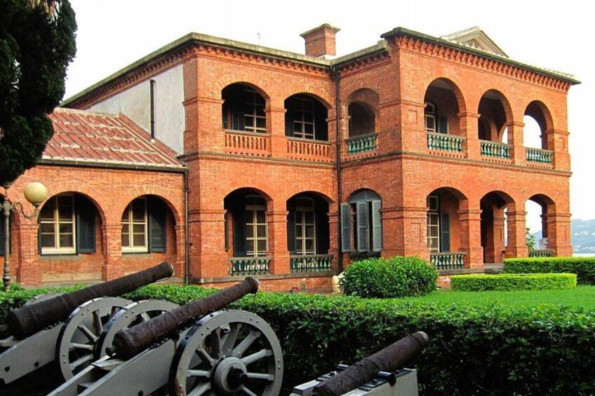 A brick building with arched windows and balconies, surrounded by well-maintained hedges. 3