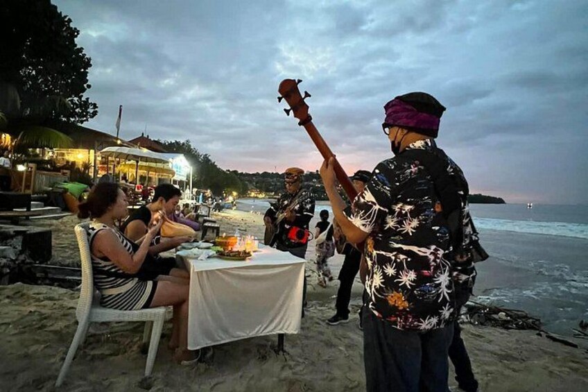 A beachside dining area with people seated at tables, a musician playing a guitar, and a view of the ocean. 5