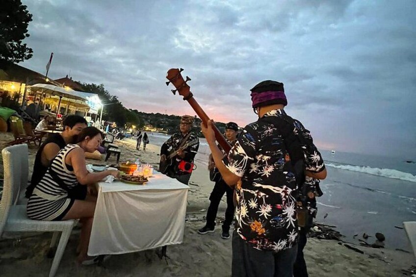 A beachside dining area with people seated at tables, a musician playing a guitar, and the ocean in the background. 3