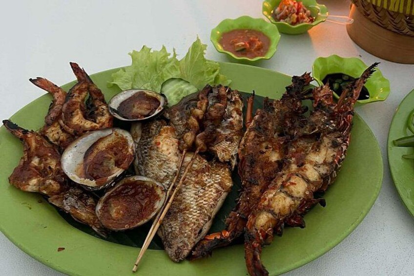A plate of grilled fish with a side of sauce and vegetables. 4