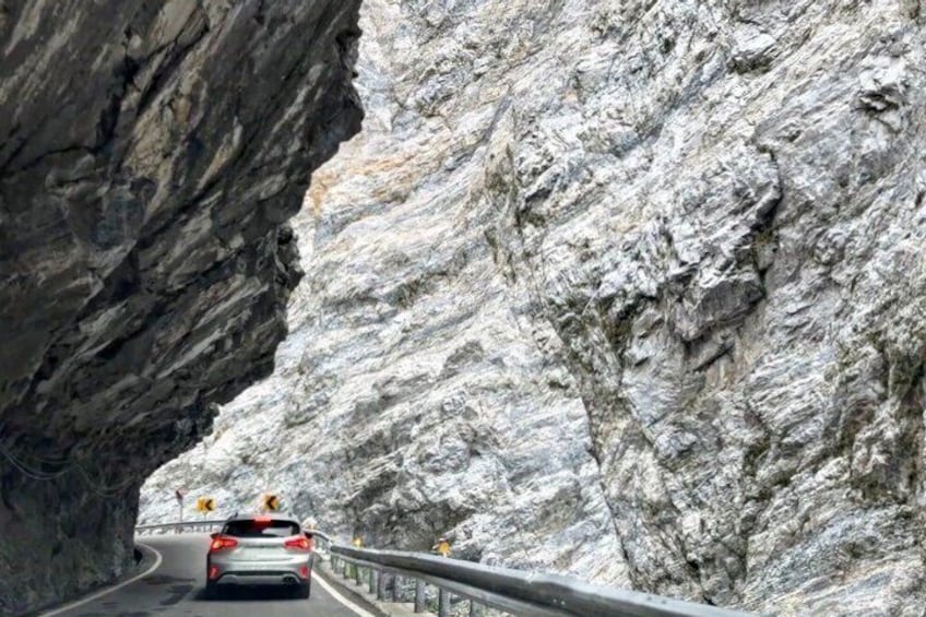 A car driving through a narrow mountain road with rocky cliffs on either side. 5