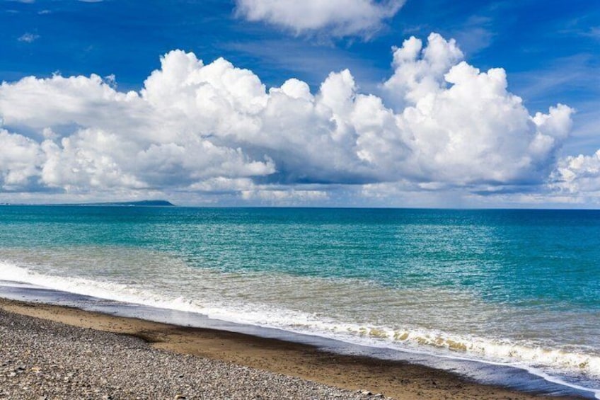 A beach with clear turquoise water, a pebbly shore, and a partly cloudy sky. 2