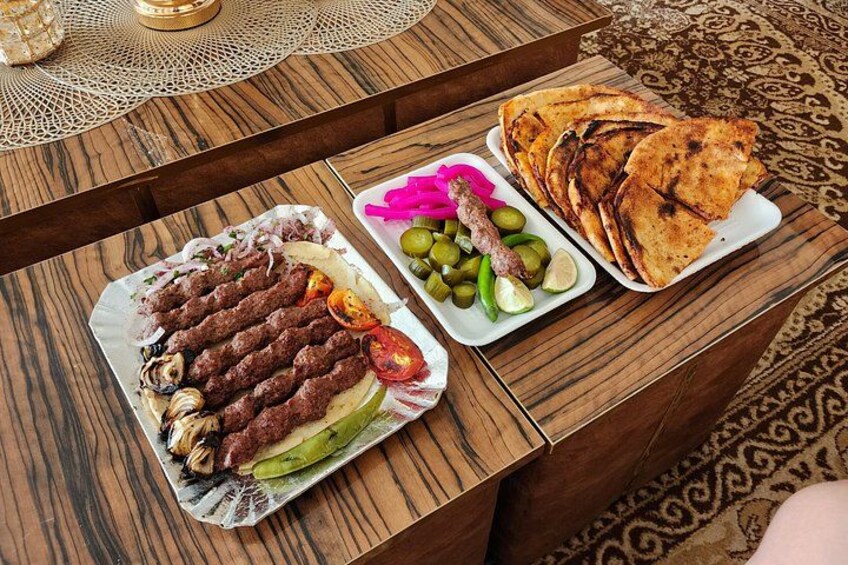 Een houten tafel met drie borden eten: kebabs, ingemaakte groenten en gegrild platbrood. 5
