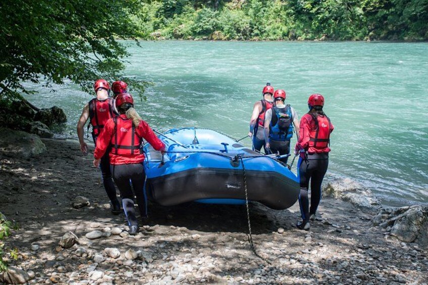 Personas con chalecos salvavidas rojos preparando una balsa azul en la orilla de un río pedregoso. 3