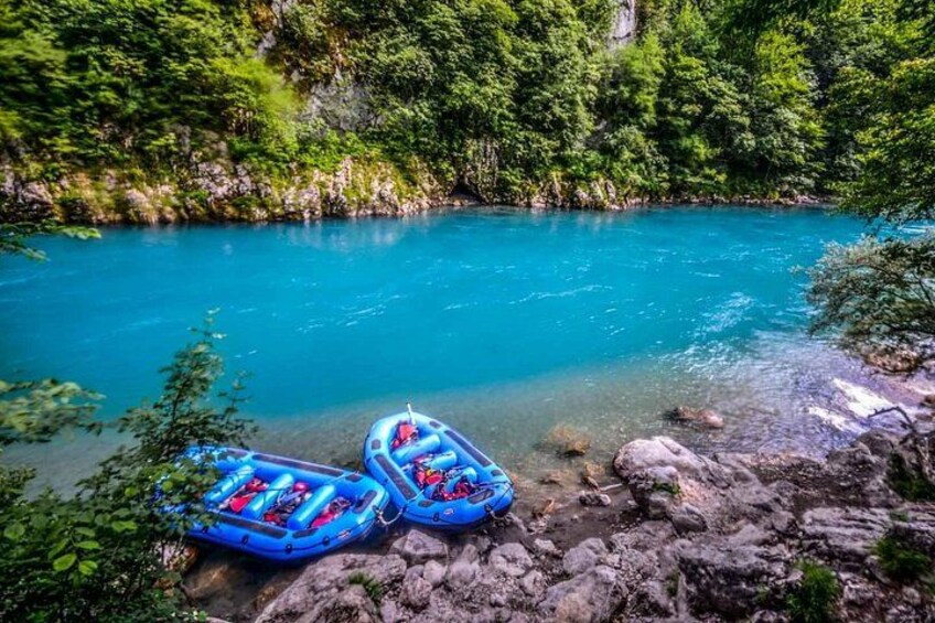 Un río azul y cristalino con dos balsas hinchables azules sobre una orilla rocosa rodeada de una vegetación verde y densa. 2
