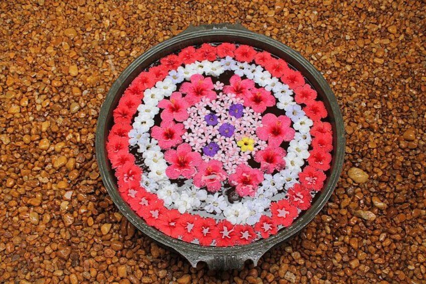 A circular flower arrangement with a central pattern of pink, white, and purple flowers, surrounded by a ring of red flowers, set on a bed of small brown pebbles. 3
