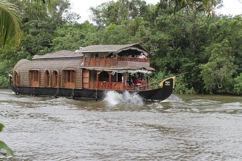 A houseboat with a wooden deck and a thatched roof, floating on a river surrounded by dense greenery. 1