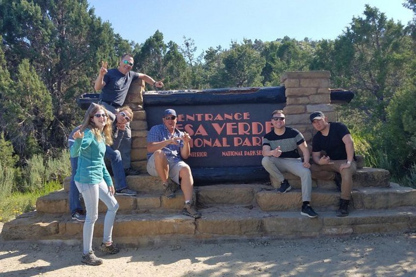 A group of people posing in front of a sign that reads 'ENTRANCE SAVE VERDE NATIONAL PARK.' 2