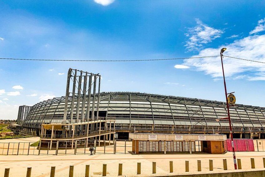 Een groot stadion in aanbouw, met een stalen constructie en een gedeeltelijk overdekt dak. 3