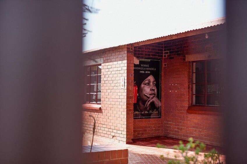 Een gebouw van baksteen met een affiche van Winnie Mandela. 5